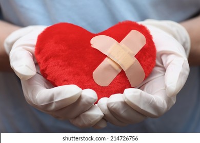 Red Heart Shape With Cross Band Aid In Doctor's Hands. Closeup.