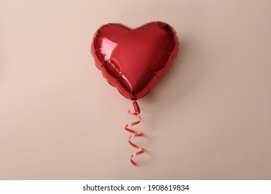 Red heart shaped balloon on beige background, top view. Saint Valentine's day celebration