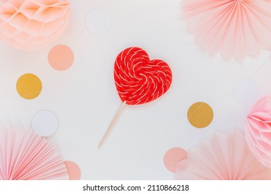 Red heart shaped candy on a pink background with paper deor, paper circles and balls. The concept of love and Valentine's day. Greeting card design for birthday, mother's day