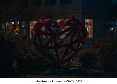 Red heart statue made of metal faintly lit during the night after a brief misting of rain 