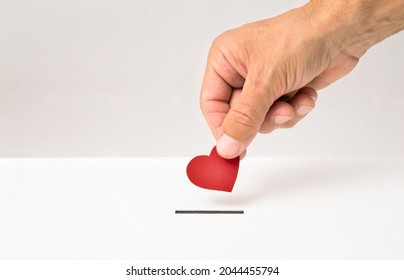 Red heart symbol is put by person's hand into slot of white donation box, Concept of donorship, life saving or charity - Shutterstock ID 2044455794