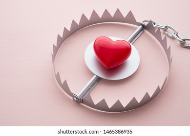 Red heart in a trap on pink background. Online internet romance scam or valentine day in darkside concept. Love is bait or victim.