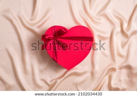Red heart-shaped box wrapped ribbon now on silk background. Happy Valentines Day concept. Flat lay, top view.