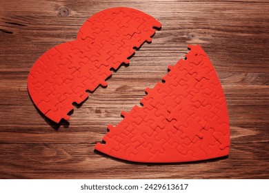 Red heart-shaped puzzle, halved and laid on a wooden surface. The fragmented pieces symbolize emotional disconnection or fractured relationships. - Powered by Shutterstock