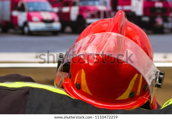 A red helmet of the firefighter against the\
background of rescue cars.  Close-up shot elements of regimentals\
of the rescuer