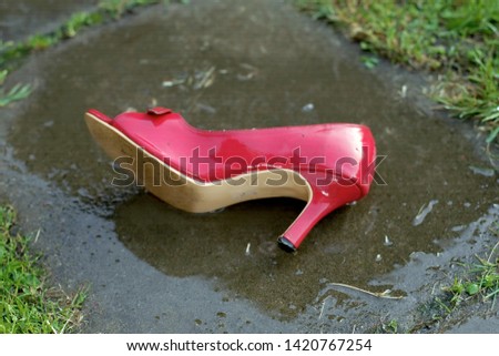 Red highheel abandoned on the asphalt, wet after rain, outdoor close-up