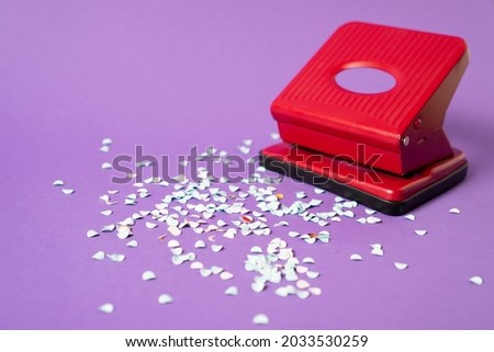 Red hole punch with a lot of paper confetti. White paper confetti from red hole puncher on violet background. High quality photo