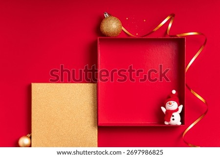 Red holiday flat lay with an empty square frame box, a golden panel, curling ribbon and ornaments. Ample copy space for seasonal mockups, banners, headers and retail showcases.