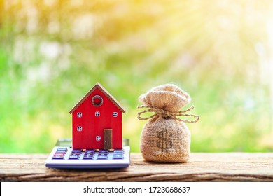 Red home model put on the calculator and money bag with presenting put on the wood in the public park, Saving money for buy house or loan for investment of real estate concept.