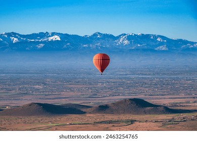 A red, hot air balloon, floating over the desert near Marrakech, Morocco on a  clear spring day, with the snow capped Atlas mountains in the background - Powered by Shutterstock