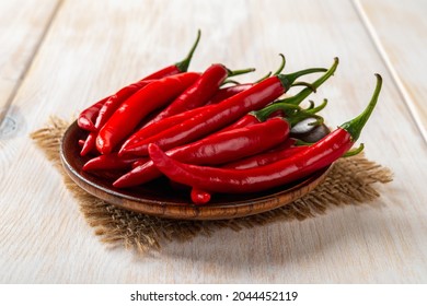 Red hot chili peppers on a brown wooden saucer over rustic table. Raw spicy chilli pepper on the plate close-up. Front view of whole fresh pungent chile or cayenne pods ready for cooking.  - Shutterstock ID 2044452119