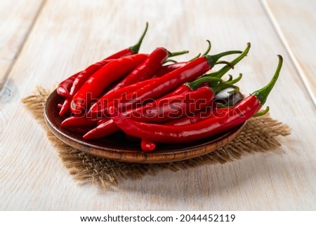 Red hot chili peppers on a brown wooden saucer over rustic table. Raw spicy chilli pepper on the plate close-up. Front view of whole fresh pungent chile or cayenne pods ready for cooking. 