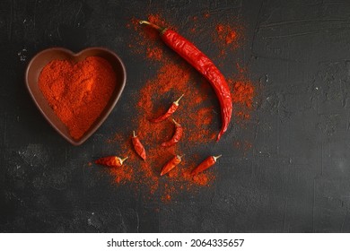 Red Hot Chili Peppers Powder In Heart Shaped Bowl On Black Stone Table. Love Concept. Top View Flat Lay With Copy Space