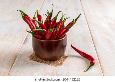 Red Hot Chili Peppers Stand Upright In A Brown Wooden Bowl Over White Rustic Table. Raw Pungent Chilli In The Ramekin Close-up. Front View Of Whole Fresh Spicy Chile Cayenne Peppers Ready For Cooking.