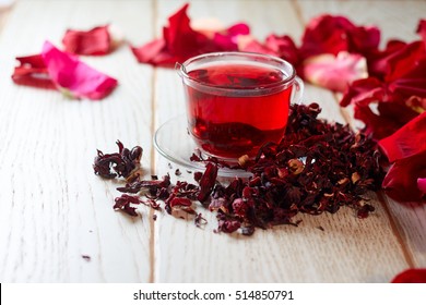 Red Hot Hibiscus tea in a glass mug on a wooden table among rose petals and dry tea custard with metallic heart