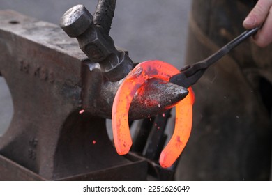 Red hot horseshoe being hammered and shaped on the anvil by the farrier. Equestrian