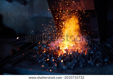Red hot metal in burning fire preparing for forging process at workshop. Sparks flying around. Traditional blacksmith manufacture.