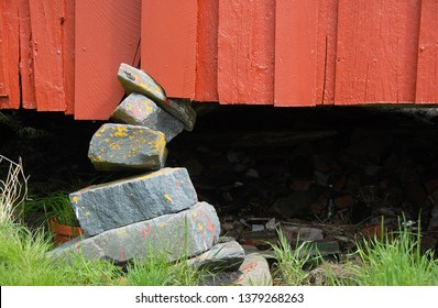 Red House Kept Up By Shaky Foundation. Close Up. Fundament Of Stacked Stones.