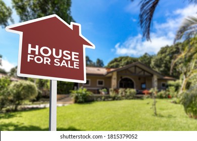 A Red House Shaped For Sale Sign In Front Of A Bungalow With A Large Lawn. Real Estate Concept.