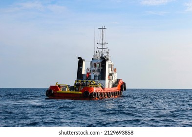 Red hulled tug boat with car tyres around it,  moving ahead in open waters. Rippled ocean surface and clear skies. - Shutterstock ID 2129693858