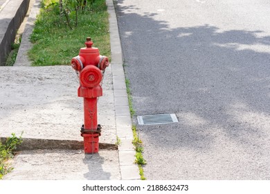 Red hydrant in harsh light on a sidewalk next to a street