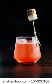 Red Iced Cocktail With Burnt Marshmallow In Drinking Glass On Wooden Table With Black Background.