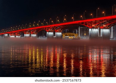 A red illuminated bridge stretches over a calm river at night, with mist floating above the water and colorful reflections. The serene urban scene captures the structure and lighting - Powered by Shutterstock