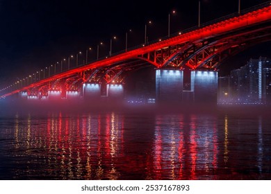 A red illuminated bridge stretches over a calm river at night, with mist floating above the water and colorful reflections. The serene urban scene captures the structure and lighting - Powered by Shutterstock