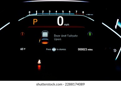 Red illuminated tailgate trunk open warning on instrument panel, dashboard control modern minivan car, low milage only 23 miles glowing LED indicator display.  Driving safely assistant technology