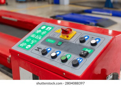 Red industrial control panel with buttons and safety symbols. Panel shows green and yellow icons for operation. Controls include red emergency stop and multiple function switches