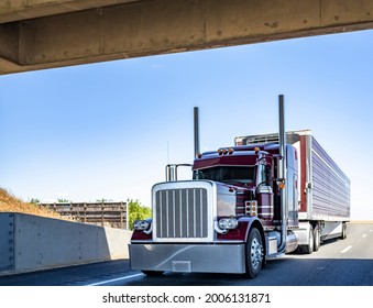 Red Industrial Long Haul Big Rig Bonnet Semi Truck With Chrome Transporting Frozen Commercial Cargo In Refrigerator Semi Trailer Running For Delivery On Wide Multiline Highway Road Under The Bridge
