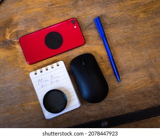 Red Iphone On Wooden Table With Computer Mouse, Notepad And Blue Pen