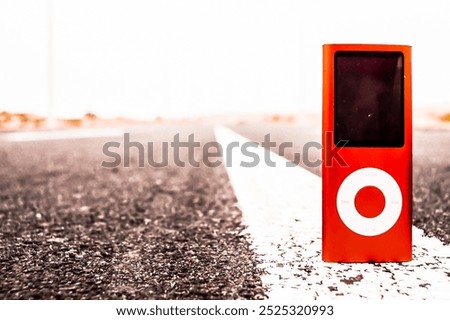 A red iPod is sitting on the side of a road. The iPod is the only object in the image