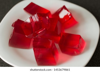 Red Jelly Cubes On White Plate Background. Berry Sweet Pieces Of Jelly. Homemade Red Cherry Gelatin Dessert.