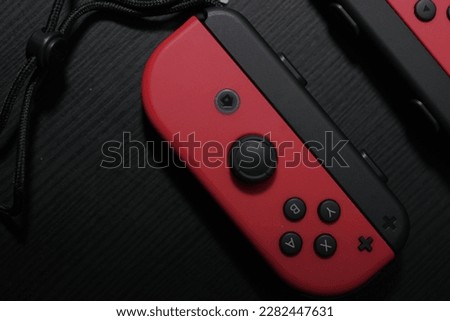Red Joycon controller on a black table. Perfect for gaming enthusiasts and Nintendo fans. This photo captures the essence of entertainment and fun.