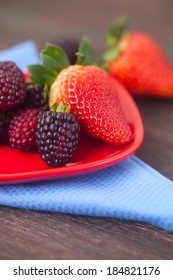 red juicy strawberry and blackberry in red plate on a wooden surface