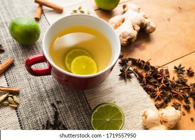 Red jumbo mug contains warm green tea and limes. Tea spices (used in chai, like whole cloves, cinnamon sticks, fresh ginger, star anises) on rustic orange wood and vinyl neutral fabric background - Powered by Shutterstock