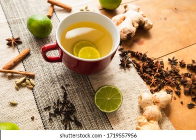 Red jumbo mug contains warm green tea and limes. Tea spices (used in chai, like whole cloves, cinnamon sticks, fresh ginger, star anises) on rustic orange wood and vinyl neutral fabric background - Powered by Shutterstock