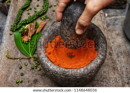 Red Kashmiri chilli powder in a mortar Kerala South India. Traditional Indian kitchen using vintage grinder for powdering spices which is used widely in curry. 