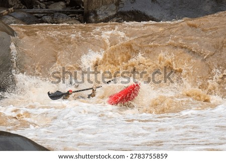 Red kayak floating upside down turbulent brown whitewater rapid with black paddle nearby feeling intense and dangerous environment showing extreme outdoor water sports accident during river flood