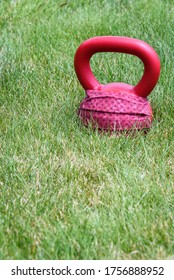 Red Kettle Bell With A Red Face Mask, On A Green Lawn, Ready For An Outdoor Workout
