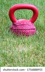 Red Kettle Bell With A Red Face Mask, On A Green Lawn, Ready For An Outdoor Workout
