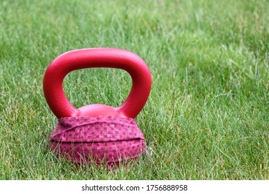 Red Kettle Bell With A Red Face Mask, On A Green Lawn, Ready For An Outdoor Workout
