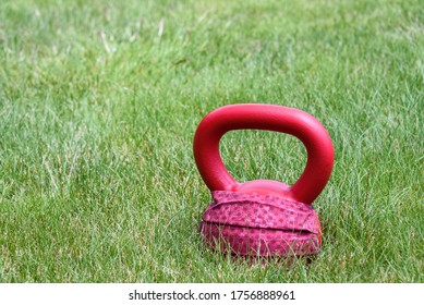 Red Kettle Bell With A Red Face Mask, On A Green Lawn, Ready For An Outdoor Workout
