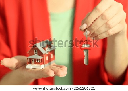 Red key and house model in hands of female manager. Concept of real estate, buy and sale house, loan and mortgage.