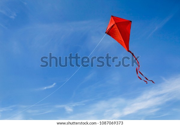 A red kite flying\
against a blue sky.