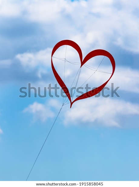 Red kite in the shape of heart in the blue sky\
with clouds at the festival of kites symbolizes love happiness in\
the wedding of a happy life