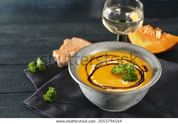 Red kuri squash soup with parsley garnish in a\
rustic blue bowl, wine and bread on a dark wooden table, autumn\
meal for Thanksgiving or Halloween, copy space, selected focus,\
narrow depth of field