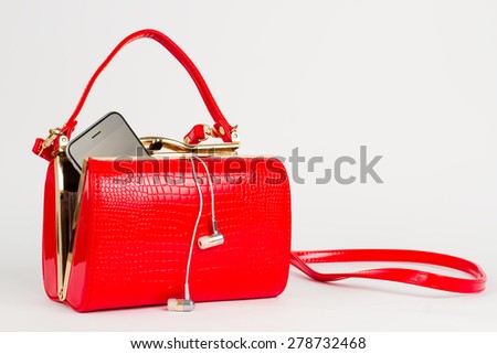 Red lacquered handbag. Phone with headset in the bag.