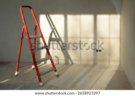 Red ladder stepladder in empty room, without renovation. Concrete wall, grey background. Repair concept. Copy space. Place for text